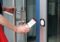 A person in a red skirt uses a smartphone to access a building by tapping it against the glass doors modern access control system, seamlessly integrating technology with security.