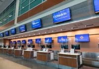 digital sinage example - An empty airport check-in area features sleek digital signage, with screens displaying @mspairport and @suncountryair next to Check-in instructions. It reminds passengers that face coverings are required. The modern space is enhanced by overhead lighting and a linoleum floor.