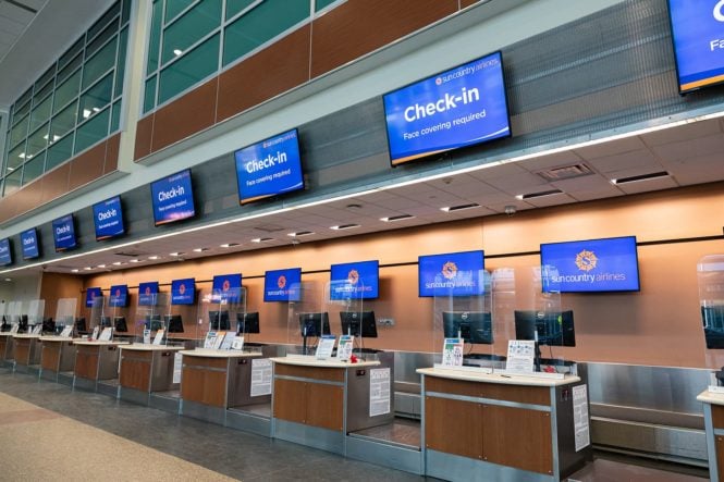 digital sinage example - An empty airport check-in area features sleek digital signage, with screens displaying @mspairport and @suncountryair next to Check-in instructions. It reminds passengers that face coverings are required. The modern space is enhanced by overhead lighting and a linoleum floor.