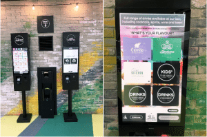 Two ACRELEC self-service kiosks sit against a colorful brick wall. The left kiosk features a digital menu, while the right screen presents drink options with Whats your flavor?—highlighting cocktails and kids drinks—enhanced by AI Voice Ordering for a seamless experience.