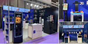 ACRELEC Spain - The exhibition booth, adorned with a purple carpet, showcases digital kiosks and screens featuring technology products. Brand logos like AURES Group, EuroCIS, and ACRELEC are prominently displayed, alongside interactive displays highlighting AI Voice Ordering and a brochure stand.