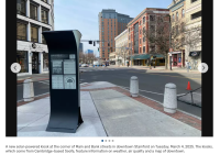 A solar-powered kiosk in downtown Stamford provides crucial wayfinding information amidst brick buildings and shops. The quiet street, free of pedestrians and vehicles, showcases the kiosks efficient design while offering real-time weather updates to passersby.