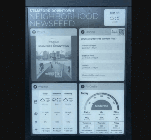 The digital display, part of Stamfords solar kiosks, features the Stamford Downtown Neighborhood Newsfeed, showcasing wayfinding information with sections including a poster for Stamford Downtown, an opinion poll on favorite comfort food, weather forecast, and a Moderate air quality index.