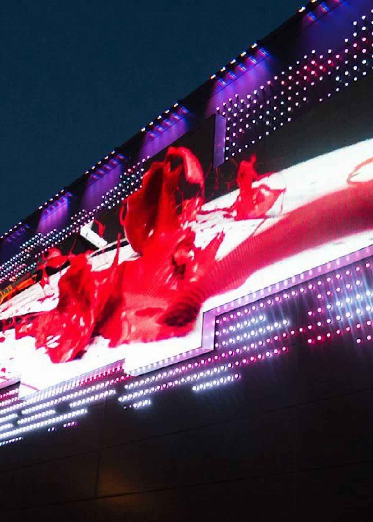 A large digital billboard showcases a vibrant red abstract image, surrounded by rows of purple and white LED lights against a dark sky—a pixel-perfect example of modern digital signage.